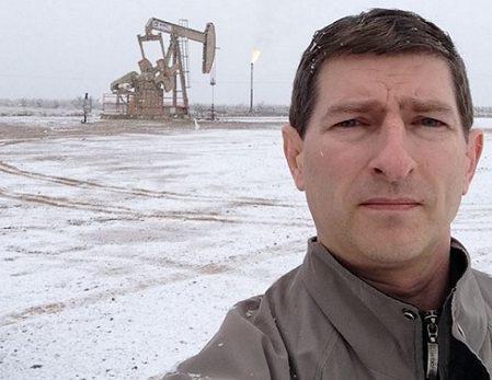 Robert Rapier standing on a snowy well pad, a pumpjack and gas flare behind him.
